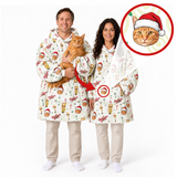A man and a woman wearing matching holiday-themed hooded robes with a festive print, standing on a white studio background. The man holds an orange tabby cat, and there is a circular inset showing a close-up of the robe's print.