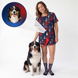 A woman wearing a custom-printed short-sleeve top and matching shorts stands next to a dog, with a circular inset showing the dog's face and arrows indicating a custom print design. The clothing features a navy blue background with cartoon dog illustrations and red hearts.