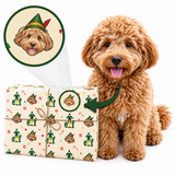 A fluffy golden-brown dog sits beside a wrapped gift box on a white background. The gift is wrapped in a cream paper with a repeating holiday print of an elf wearing a green hat, candy canes, and paw prints.