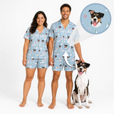 A man and a woman wearing matching light blue pajama sets with a dog print, standing barefoot on a white studio background next to a black and white dog. A circular inset shows a dog portrait that appears inside the pajama print.