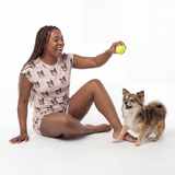 Woman wearing fitted pajama set sitting on the floor with a small dog, holding a yellow ball
