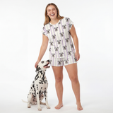Woman wearing a fitted pajama set standing next to a Dalmatian dog on a white background