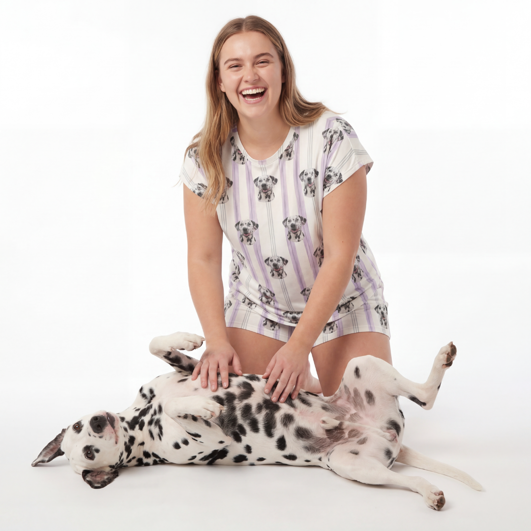 Woman in a lilac stripes pajama set sitting next to a Dalmatian dog on a white background