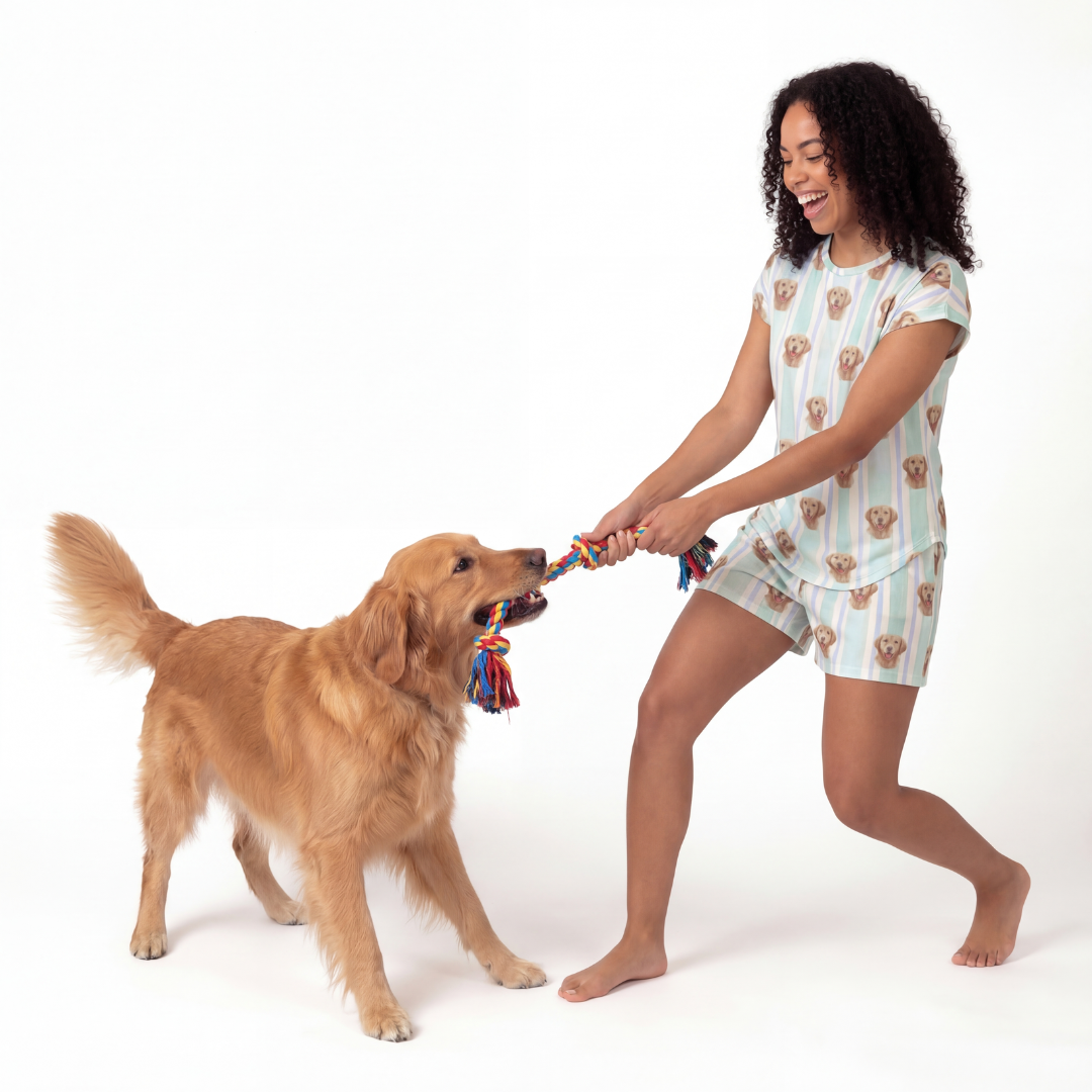 Woman in fitted pajama set playing tug with a dog on a white background