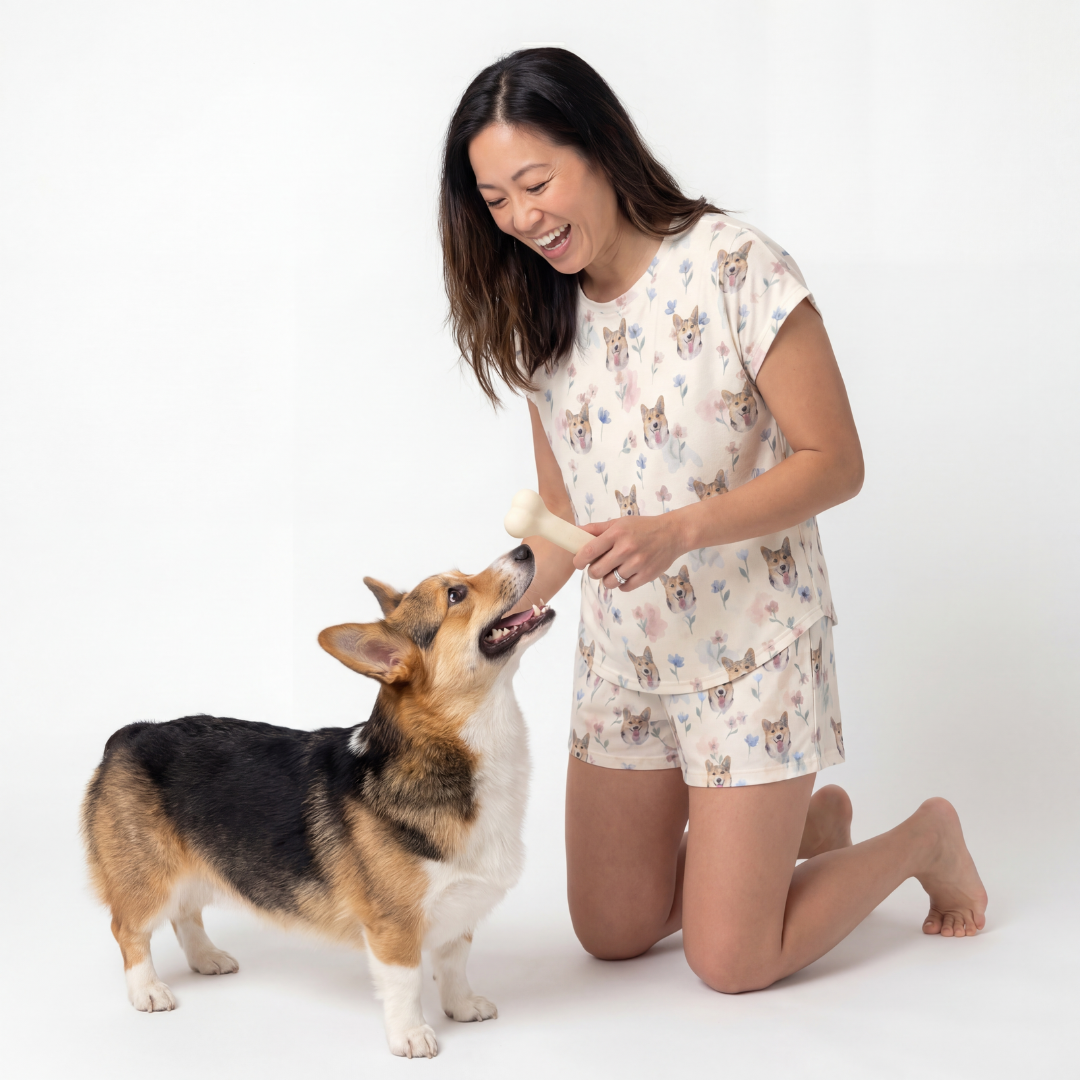 Woman in fitted pajamas kneeling on a white background with a corgi dog.
