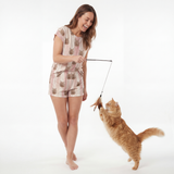 Woman wearing fitted pajama set in a cat-themed outfit playing with a cat toy against a white background