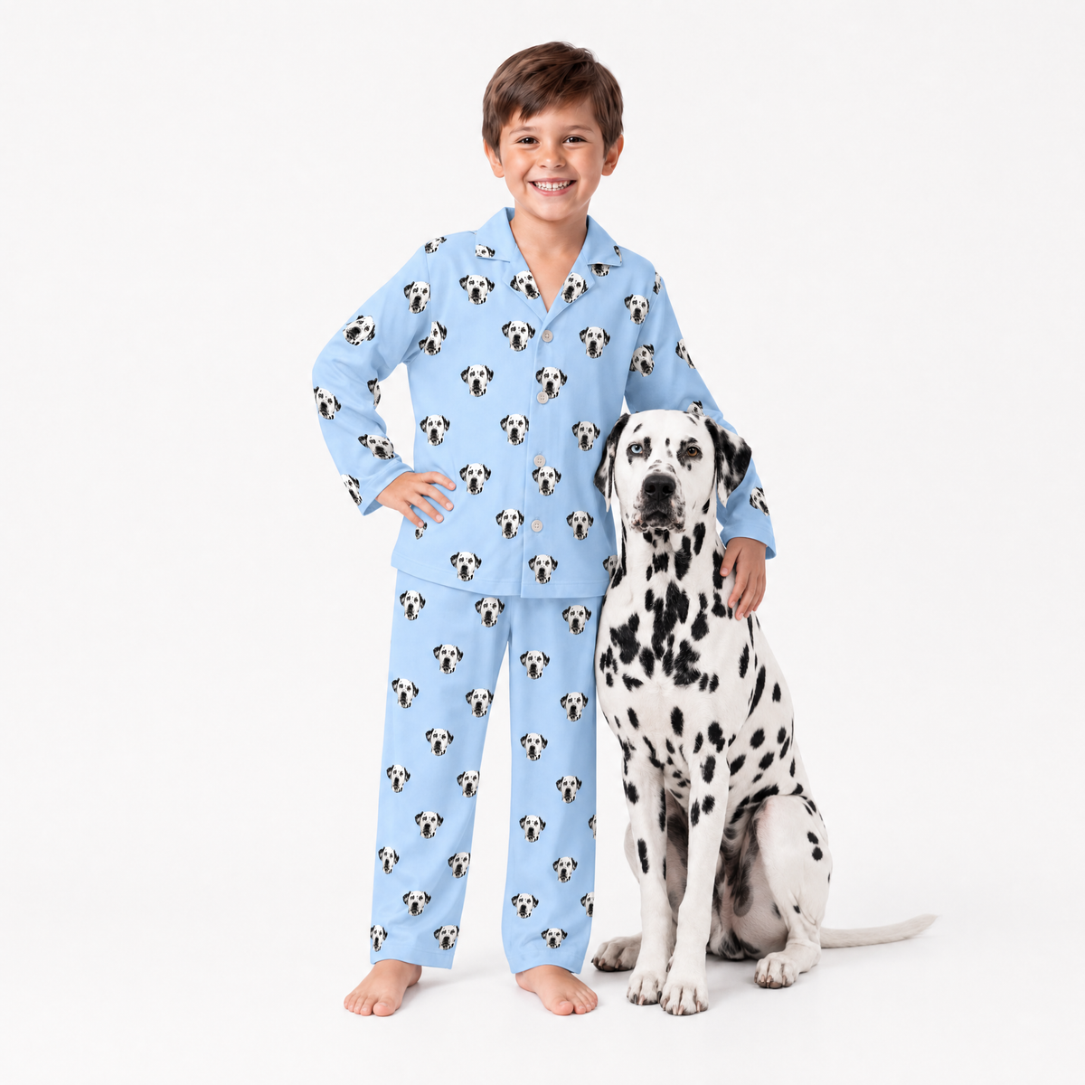 Child wearing sky blue pajamas with dalmatian pattern standing next to a Dalmatian dog on a white background