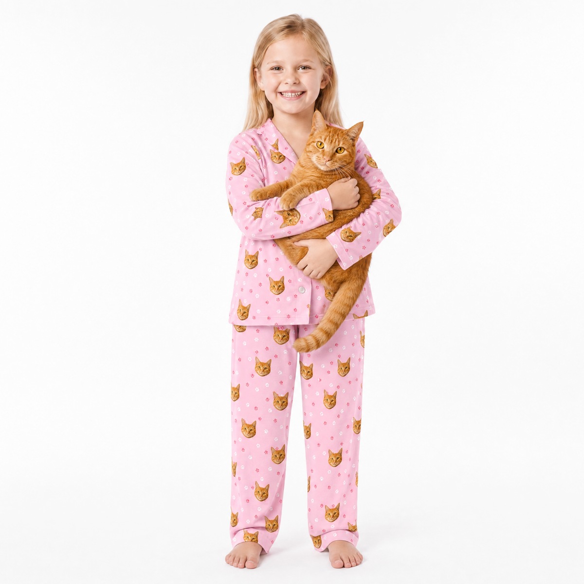 Child wearing pink pajamas with cat pattern holding a cat on a white background