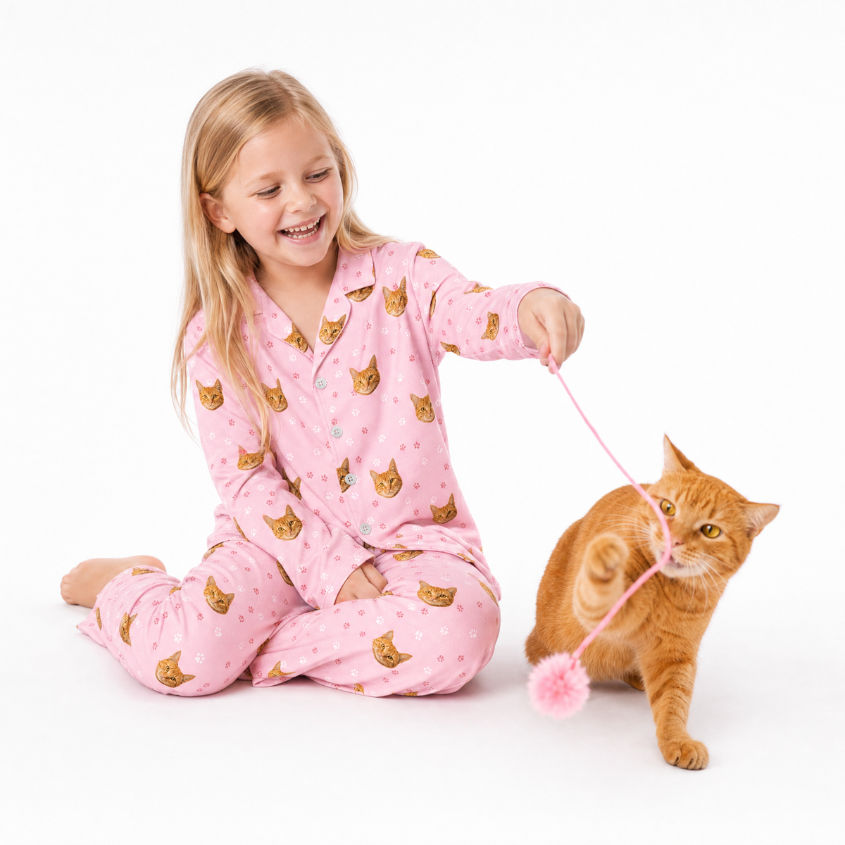 Child in pink pajamas with cat pattern playing with a cat on a white background