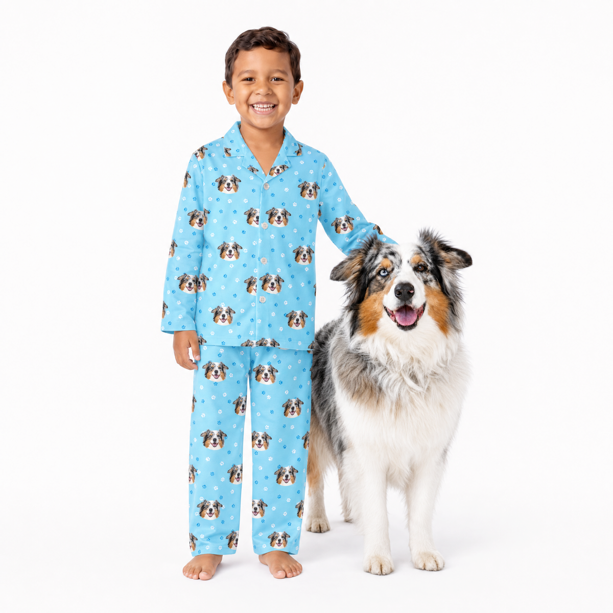 Child wearing light blue pajamas with dog pattern standing next to a dog on a white background