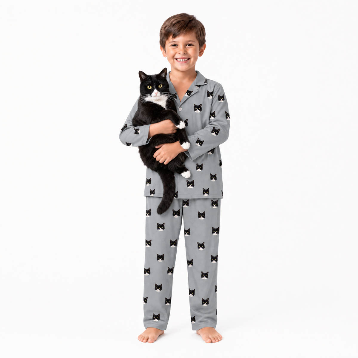 Child wearing gray pajamas with black cat pattern, holding a black and white cat on a white background