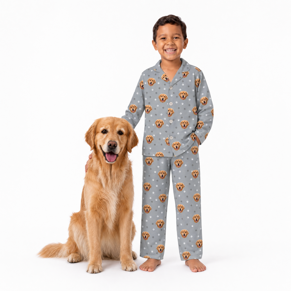 Child wearing a gray pajama set with dog pattern standing next to a golden retriever on a white background