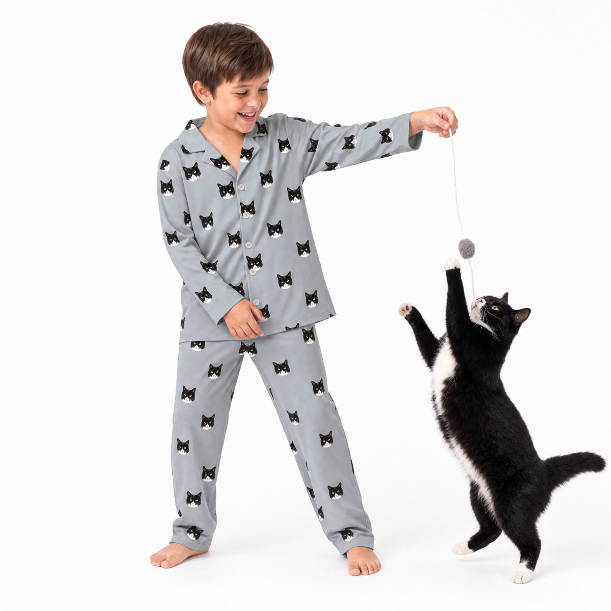 Child in gray pajama set with black cat pattern playing with a cat toy on a white background