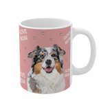 Clos up of a pink ceramic mug with hearts and the phrase "I Love Mom", featuring a smiling, multicolored Australian Shepherd