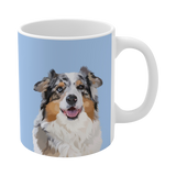A clean product shot of a blue ceramic mug featuring a smiling, multicolored Australian Shepherd