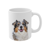 Close up of a white ceramic mug with, featuring a smiling, multicolored Australian Shepherd