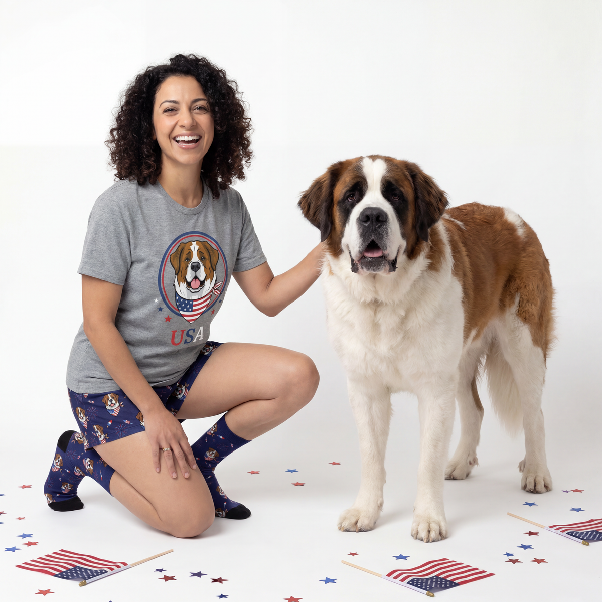 Woman wearing a t-shirt with a dog graphic and USA text, kneeling next to a large dog on a white background with American flags.