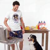 Man grilling outdoors with a dog, table with food, and American flags in the background