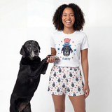 Woman wearing a t-shirt with a dog graphic and shorts, standing next to a black dog on a white background