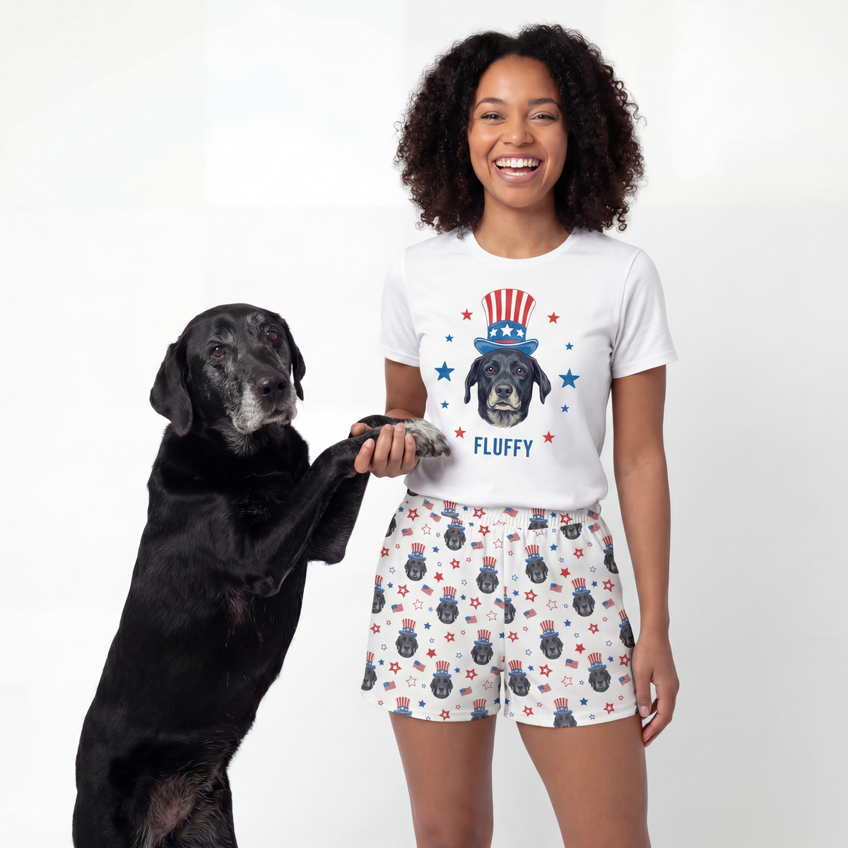 Woman wearing a t-shirt with a dog graphic and shorts, standing next to a black dog on a white background
