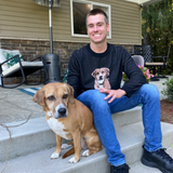 Man wearing a black knit sweater sitting next to his dog