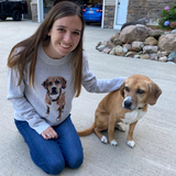 Woman wearing a knit sweater with a dog in the center, she is next to her dog.