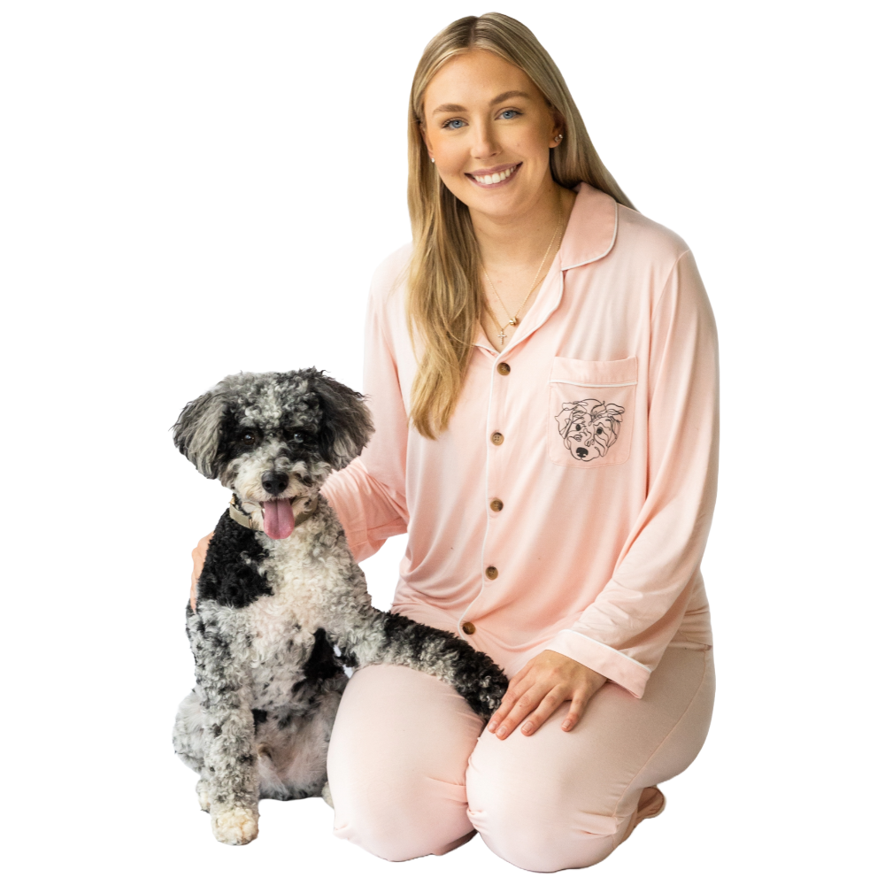 A woman in a pink bamboo pajama set with short sleeves and pants, sitting next to a dog. 