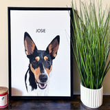 Framed 'Josie' dog portrait on a wooden surface beside a green plant and a candle.