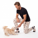 Man in pajama sweatpants with socks  kneeling on a white background with a small dog.