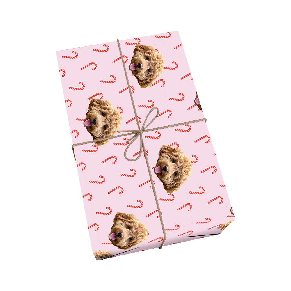 Custom pet wrapping paper in light pink with dog portraits and red and white striped candy canes with golden ribbon accent