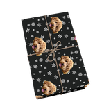 Black pet wrapping paper with dog portraits, white snowflakes, and a golden ribbon.