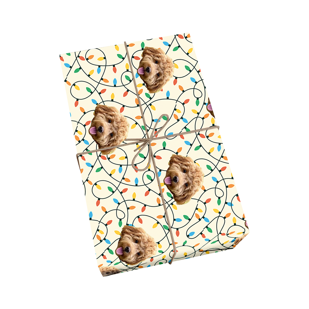 Custom pet wrapping paper in cream color with dog portraits and colorful string Christmas lights in red, yellow, blue, and green with golden ribbon accent