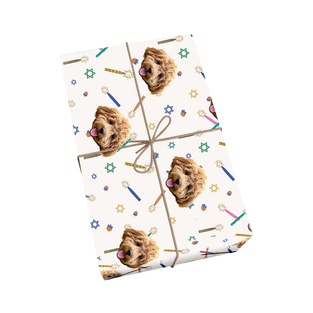 Custom pet wrapping paper in white featuring repeating pattern of dog portraits with Hanukkah symbols including Stars of David, menorahs, dreidels, and colorful candles with golden ribbon design